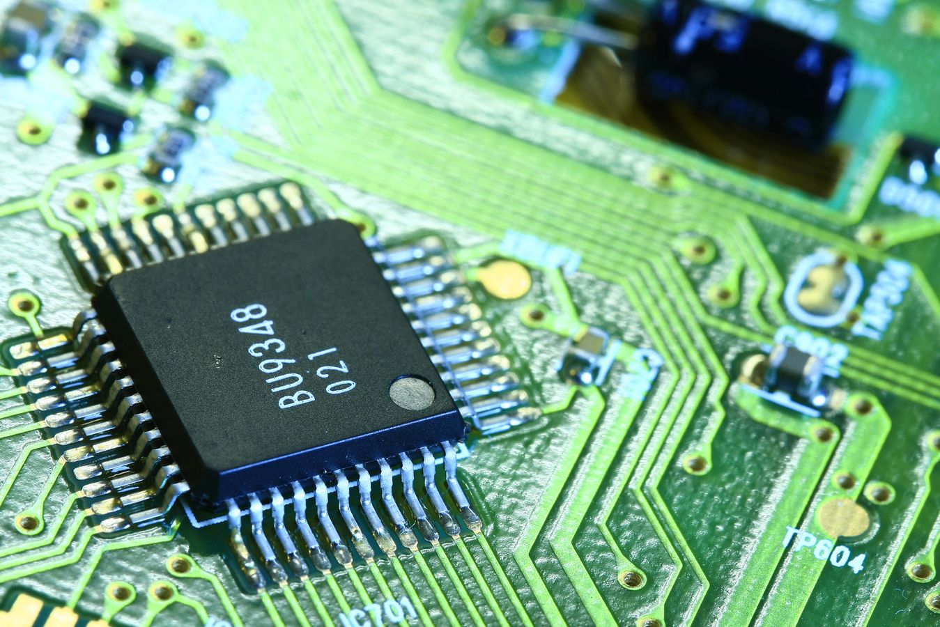 Nahaufnahme eines grünen Leiterplattenbereichs mit einem schwarzen Mikrochip und sichtbaren Leiterbahnen